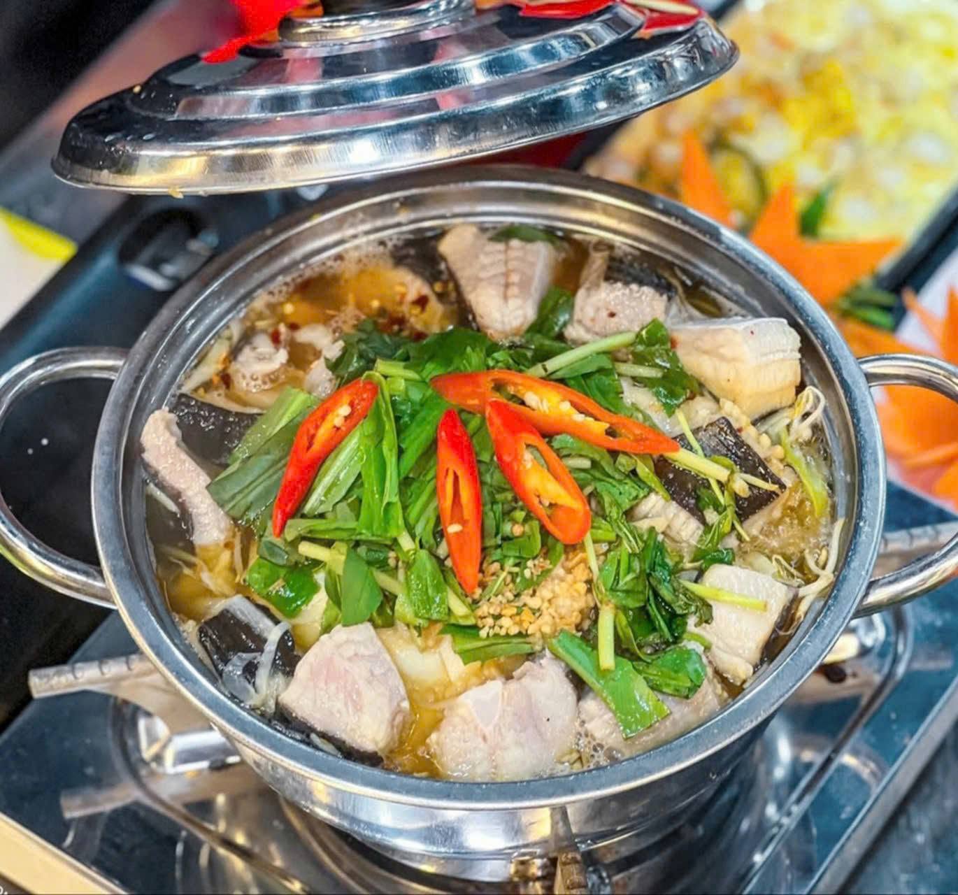 Nồi lẩu cá đuối với rau và ớt trên bếp tại bàn